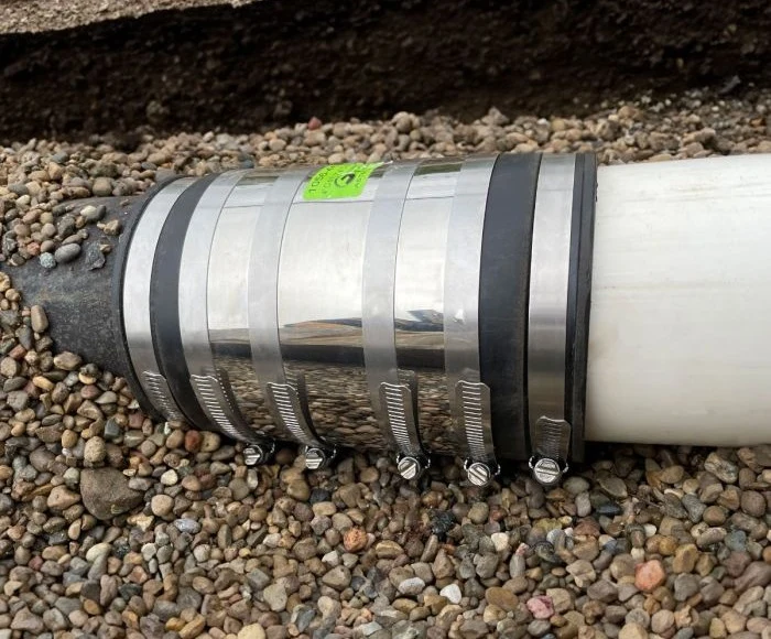 Fernco 4 inch XL Strong Back RC coupling joining cast iron to PVC on gravel bedding