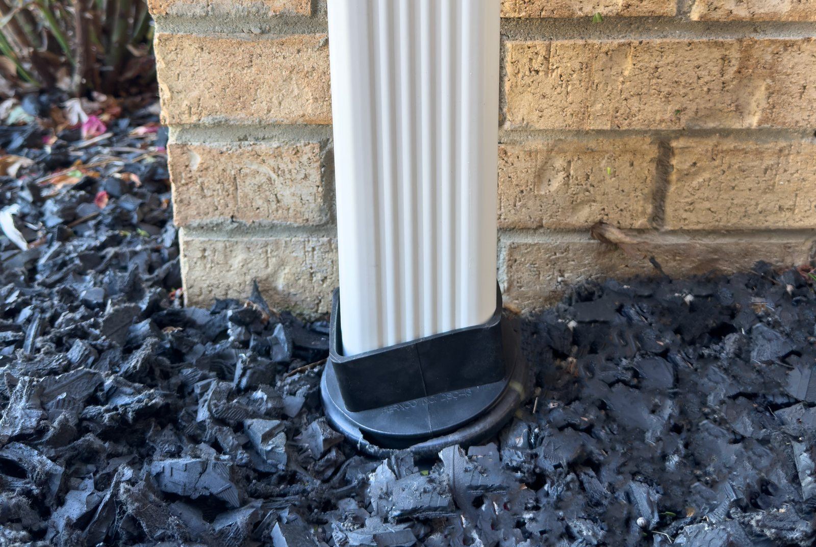 Fernco DSC-43 downspout connector joining a white downspout to an underground drain line beside a brick wall