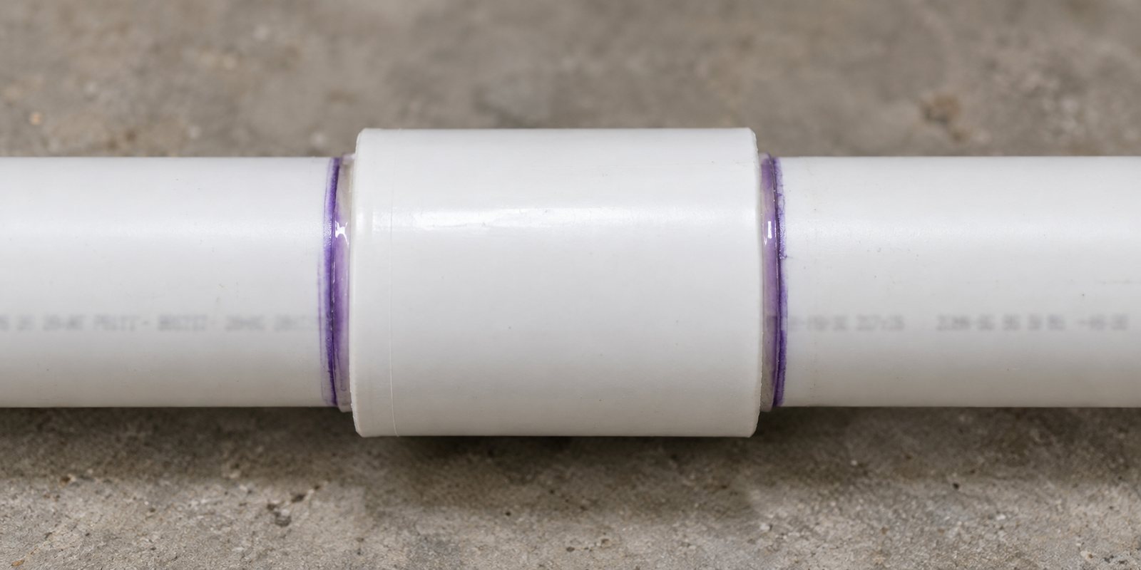 White PVC pipe solvent welded into a coupling, with purple primer at each joint