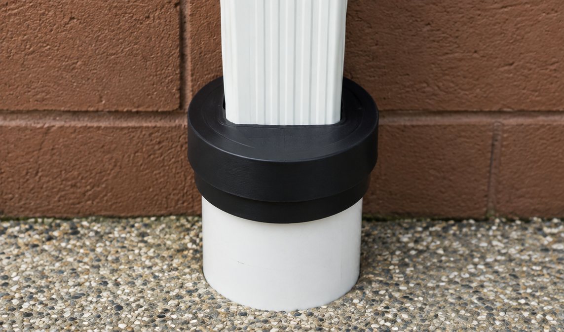 Fernco UDSC-6C cap fitted over a white 6 inch pipe above ground, with a white downspout through the top